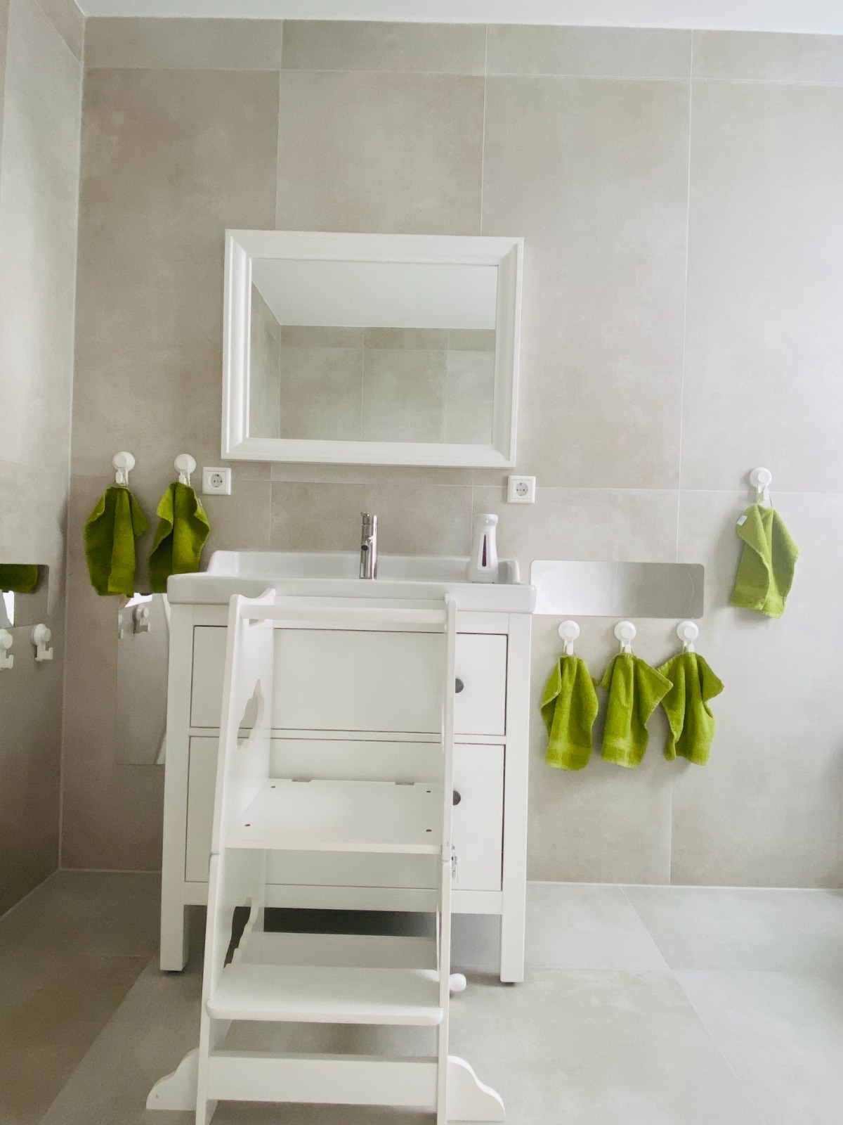 Kindgerechtes Badezimmer mit Treppchen zum Waschbecken und grünen Handtüchern